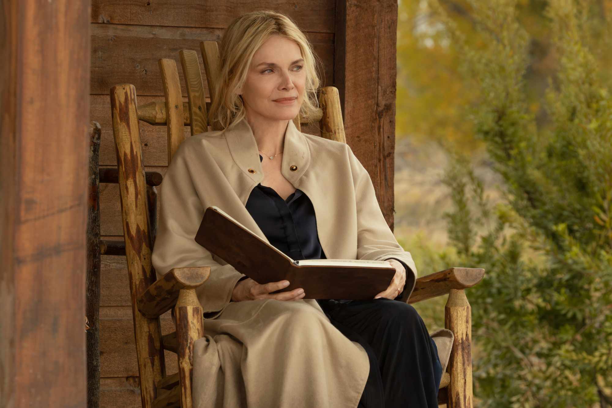 Michelle Pfeiffer sitting in a wooden chair holding an open book