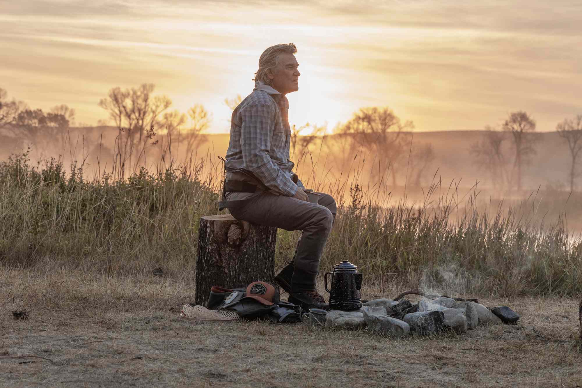 A man sitting by a campfire near a lake at sunrise