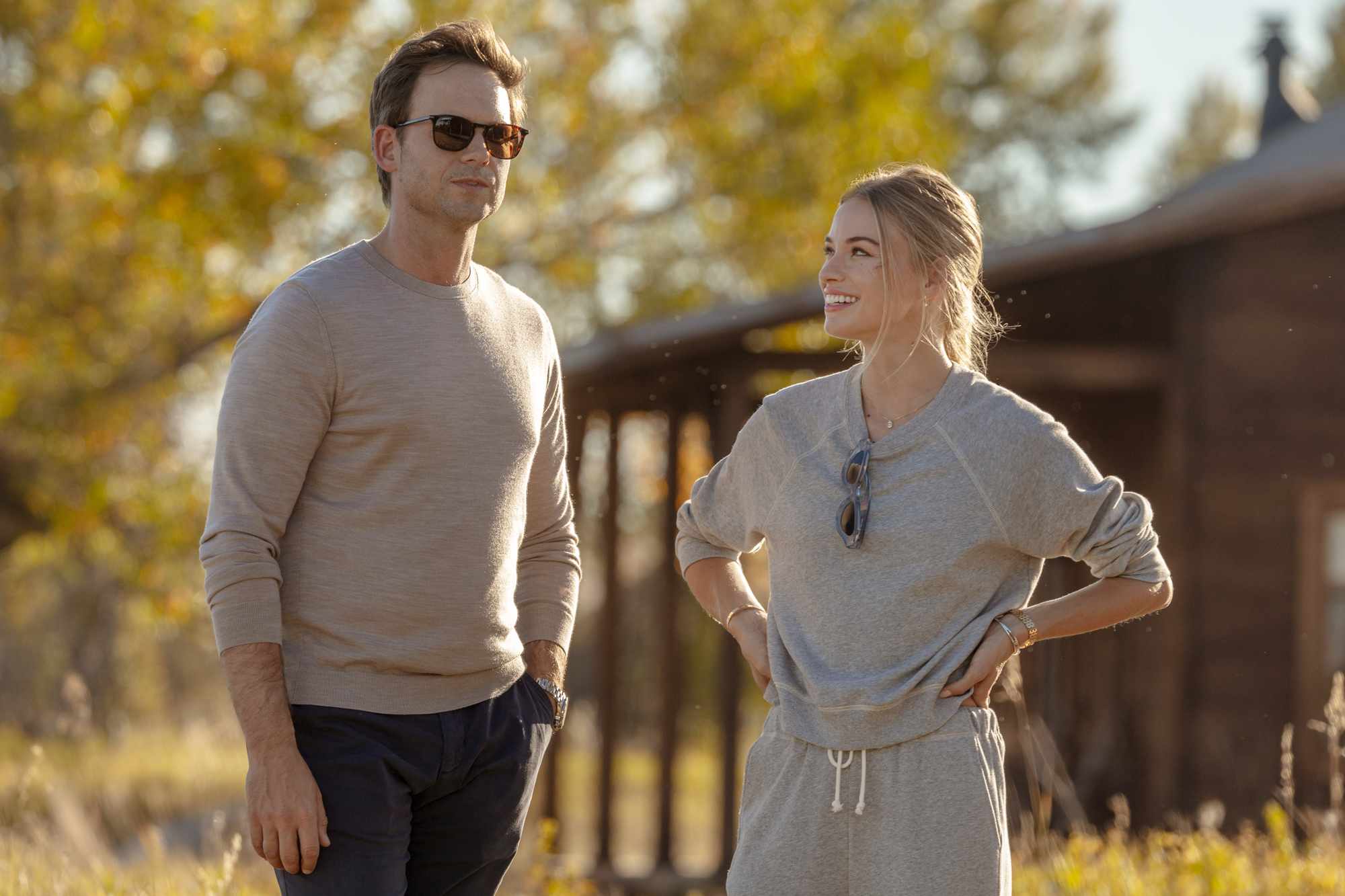 Patrick J Adams outdoors with another individual standing near a wooden building