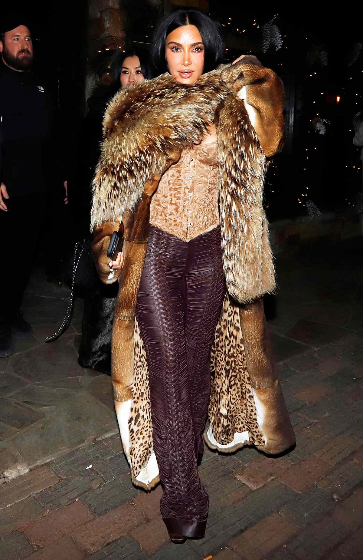 Kim Kardashian, 45, exiting Prada in Aspen on January 1, 2026, wearing a long fur coat over a tan corset and burgundy leather trousers.